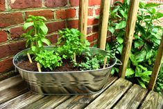 a metal tub filled with plants on top of a wooden table next to a brick wall