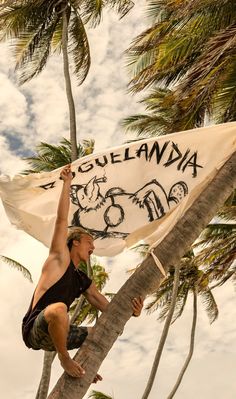 a man climbing up the side of a palm tree with a flag in his hand