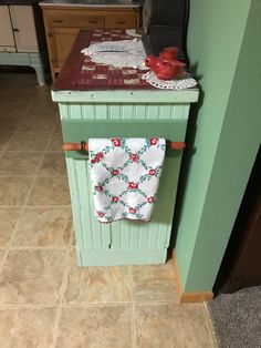 a kitchen with green cabinets and tile flooring in the center is a teal colored island that has two towels hanging on it