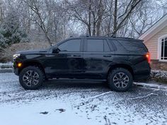 a black suv parked in front of a house on a snow covered driveway next to trees