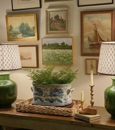 two green vases sitting on top of a wooden table next to lamps and pictures