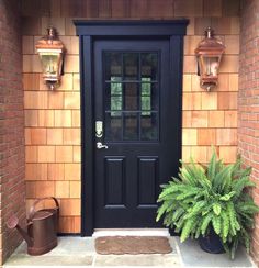 a black front door with two lights on the side and a potted plant next to it