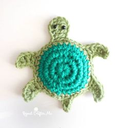 a crocheted green turtle with a blue shell on it's back, sitting in front of a white wall