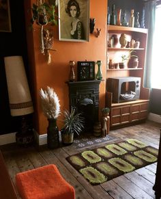 a living room with orange walls and wooden flooring, an old fashioned fireplace is in the corner