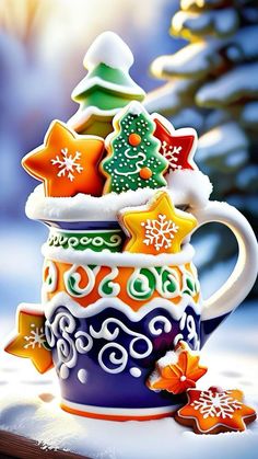 a cup filled with different types of decorated cookies on top of snow covered ground next to a christmas tree