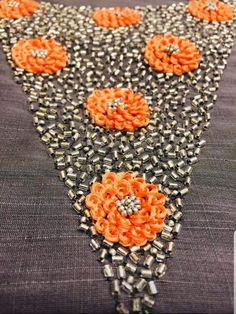 an orange and black beaded necklace with flowers on the front, sitting on a piece of fabric