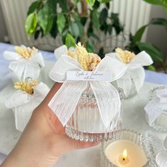 a person holding a small glass jar with flowers in it on a table next to candles