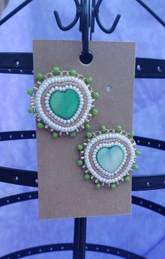 the earrings are made with green beads and white seed beadings, which is attached to a brown card