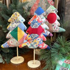 three small christmas trees made out of fabric on wooden sticks with pine cones in the background