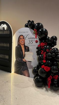 a woman holding a birthday cake in front of a welcome sign and balloon arch with roses on it