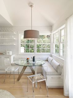 a white room with a glass table and bench next to a window in the corner