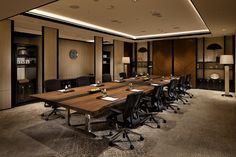 an empty conference room with wooden tables and black chairs in the center is lit by recessed lighting