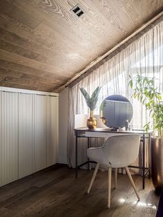 a room with a desk and chair in the corner, next to a potted plant