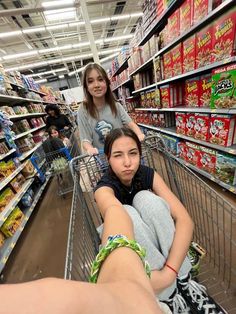 two women pushing a shopping cart through a grocery store aisle with their feet on the ground