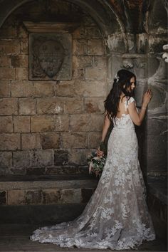 a woman in a wedding dress standing next to a stone wall