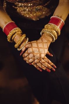 a woman's hands with gold and red bracelets