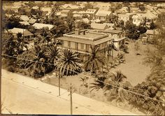 an old black and white photo of a house in the middle of town with palm trees