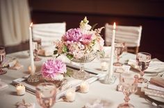 the table is set with white linens and silverware, pink flowers are in vases