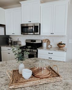 a kitchen with white cabinets and granite counter tops, including a wooden tray on the center island