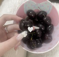 a person holding a small heart shaped object in front of a bowl of cherries