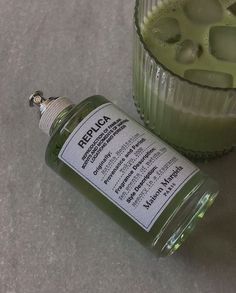 a bottle of liquid sitting next to a glass filled with green liquid and another drink in the background