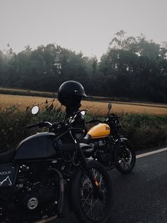 two motorcycles parked next to each other on the side of the road with trees in the background