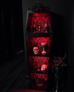 a red lighted display case with skulls and candles on it's sides in a dark room