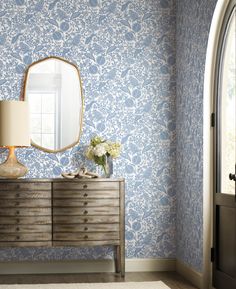 a dresser with a mirror on top of it next to a wallpapered room