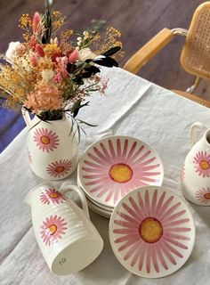 a white table topped with pink and yellow dishes next to a vase filled with flowers