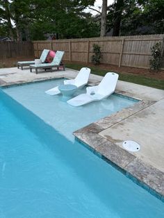 an empty swimming pool with two lawn chairs next to it and a bench in the background