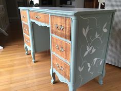 an old dresser painted in blue and white with flowers on the top, sitting on a hard wood floor