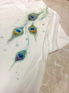 a white t - shirt with peacock feathers on it