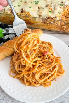 someone is holding a fork full of spaghetti on a white plate with a casserole dish in the background