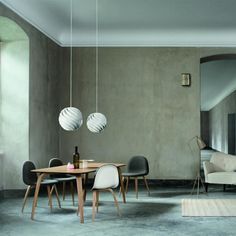 a dining room table with chairs and two lamps hanging from it's ceiling, next to a couch