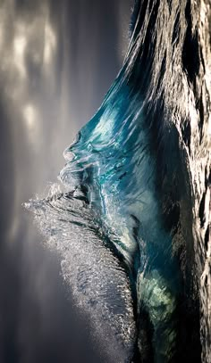 an ocean wave breaking into the water with sunlight coming through it and clouds in the background