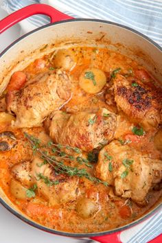 a red pot filled with chicken and potatoes