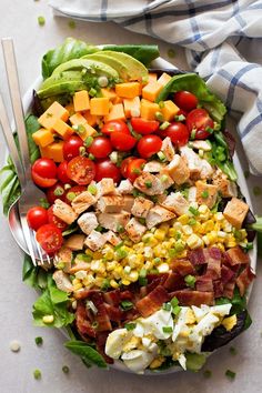 a salad with bacon, lettuce, tomatoes, corn and avocado