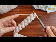 someone crocheting a piece of white yarn on a table with flowers in the background