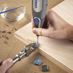 a person is using a drill to cut glass pieces on a wooden table with other tools