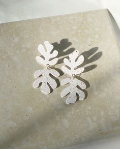 two pairs of earrings with leaves on them sitting on top of a marble slabd surface