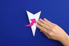 someone is cutting out an origami arrow on a blue background with pink paper