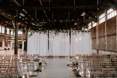 an indoor wedding venue with rows of chairs and candles on the aisle, decorated with greenery