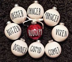 christmas ornaments with words written on them are arranged in the shape of a circle, including one red ornament and six white glass baubs