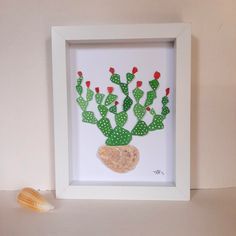 a cactus made out of paper sitting in a white frame next to a seashell