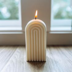 a white candle sitting on top of a wooden table next to a window sill