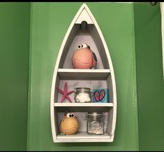 a boat shaped shelf with various items on it's shelves in front of a green wall