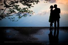 a couple standing next to each other in front of water