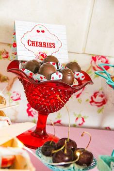 a red glass bowl filled with chocolates on top of a pink tablecloth covered table