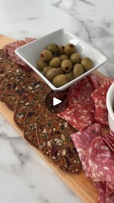 two bowls of olives and crackers sit on a cutting board next to an appetizer