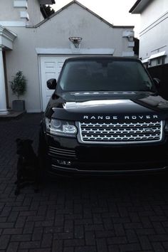 a range rover parked in front of a house with a dog sitting next to it